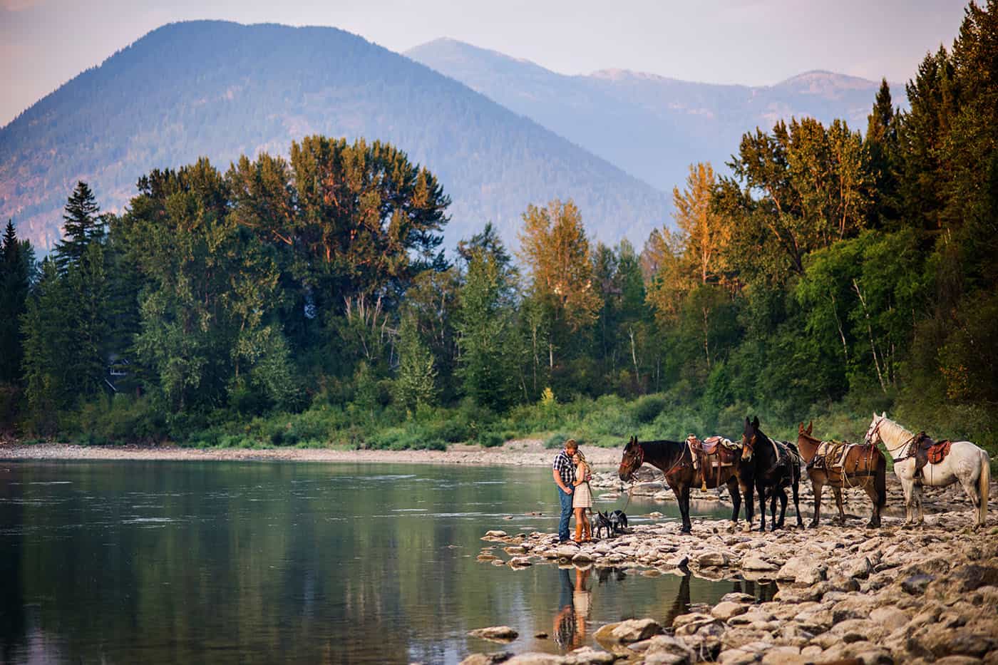 Epic Montana Photo Locations - beautiful couple with horses by a river at sunset