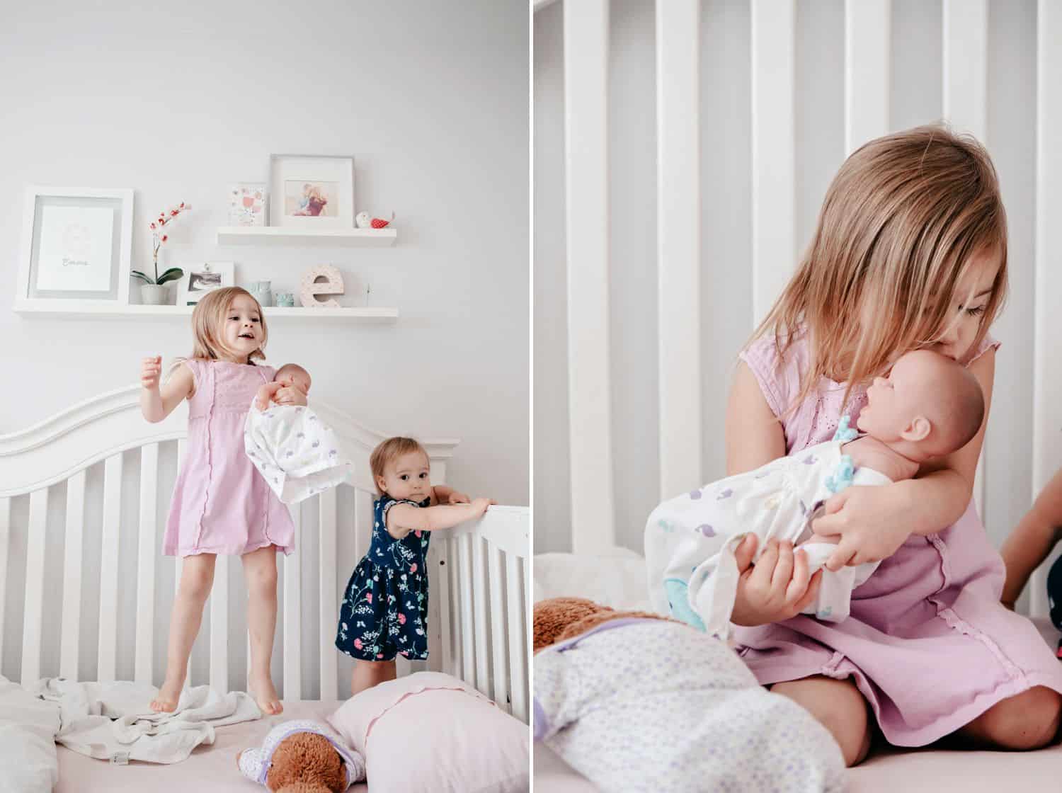Sisters play in their baby sibling's crib with a doll.