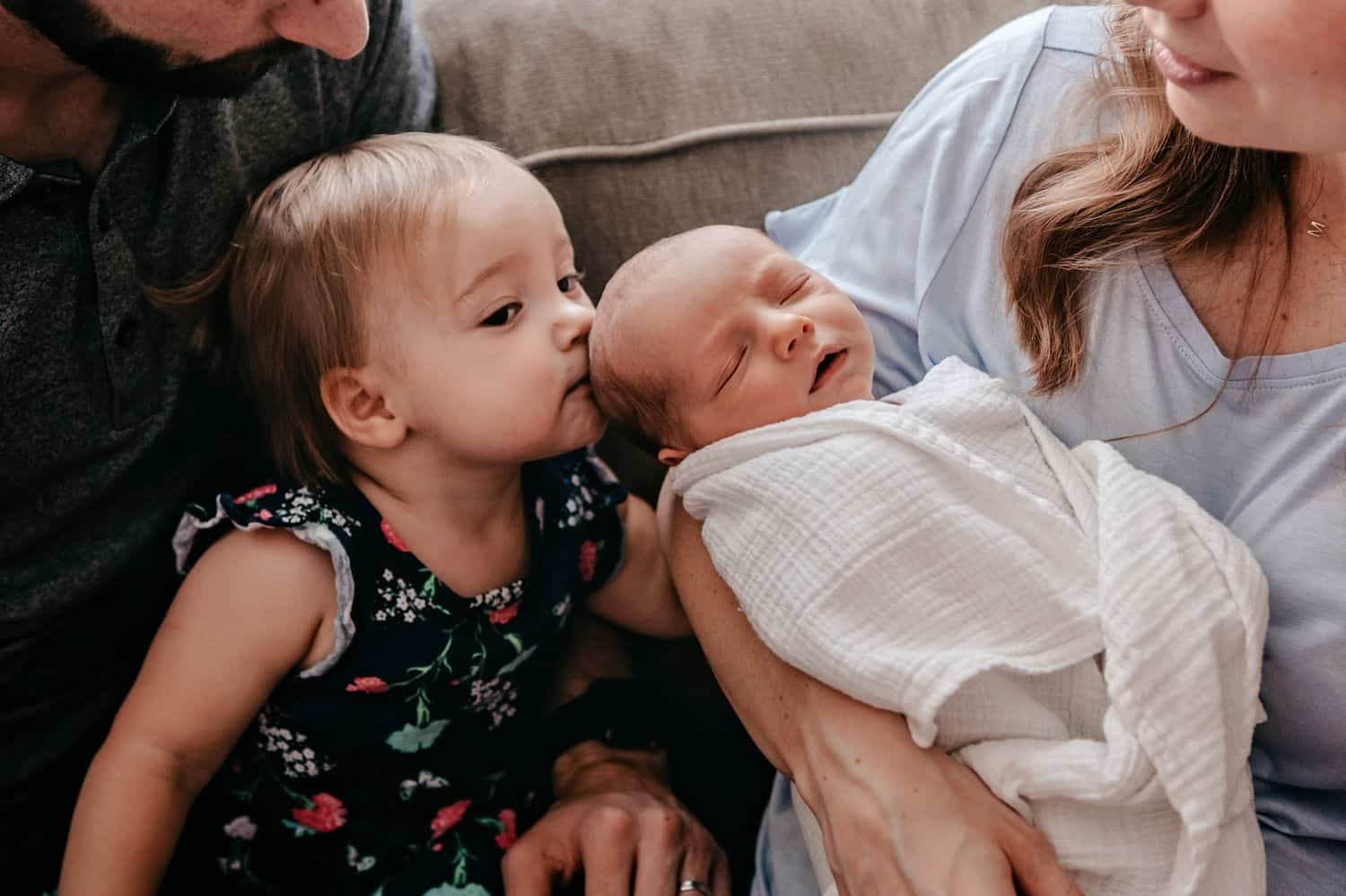 Mom holds a newborn baby so his sister can kiss him on the head.