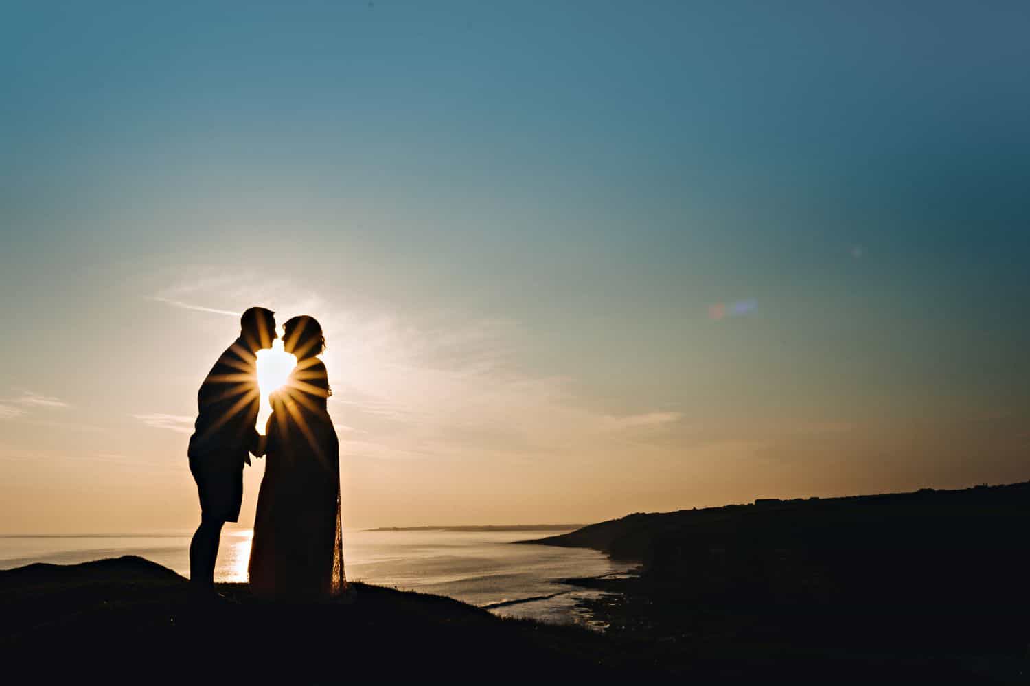 Silhouette of a man kissing a pregnant woman. They are illuminated by sunflare.
