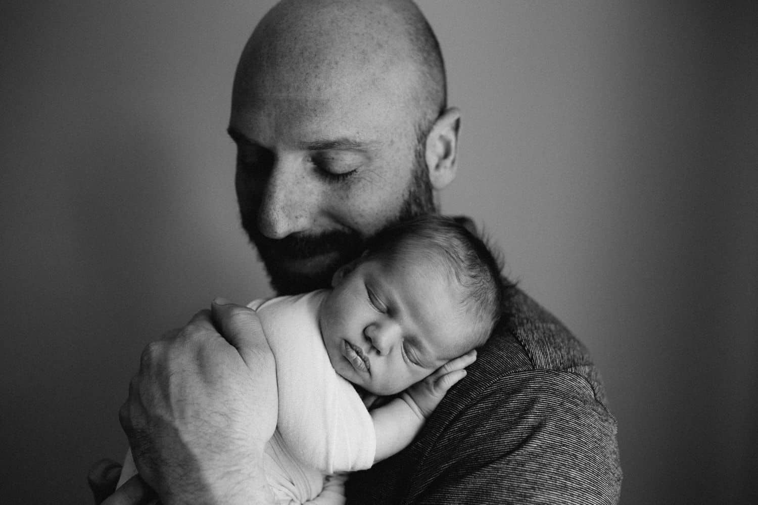 Black and white photo of a father holding his newborn baby close to his cheek.