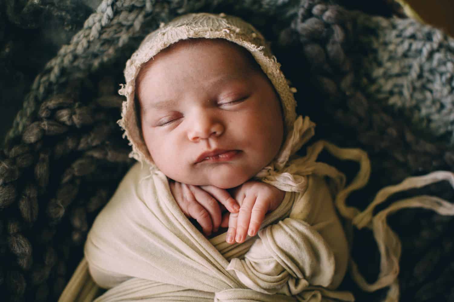 A newborn baby sleeps swaddled in linen blankets.