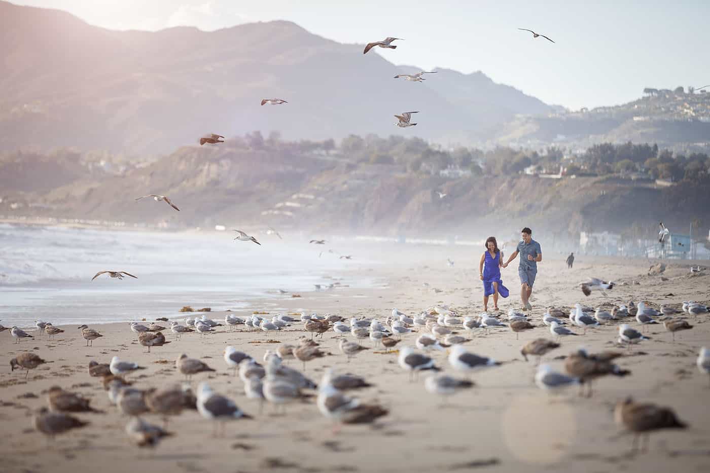 This is the Key to Amazing Client Relationships | A newly engaged couple runs along the shore of a seagull-nested beach.