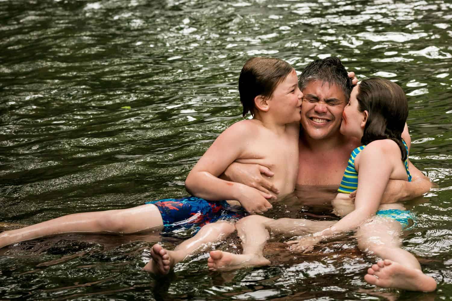 Kids kiss dad on the cheeks as they swim in the lake.