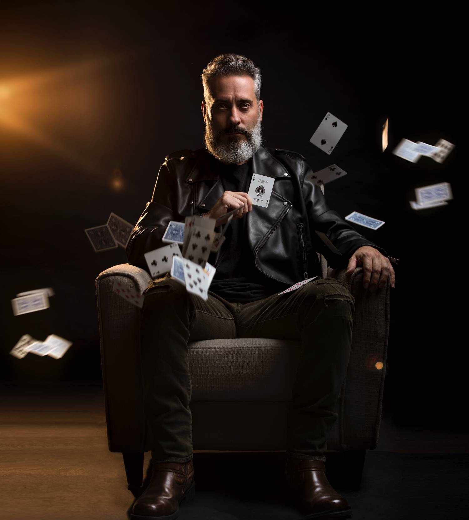 In this styled tribute photograph by Alexander Worth of Jawfox Photography, a man cosplays Negan from The Walking Dead, wearing Alton Brown clothing and seated in a leather chair as playing cards fall down around him.