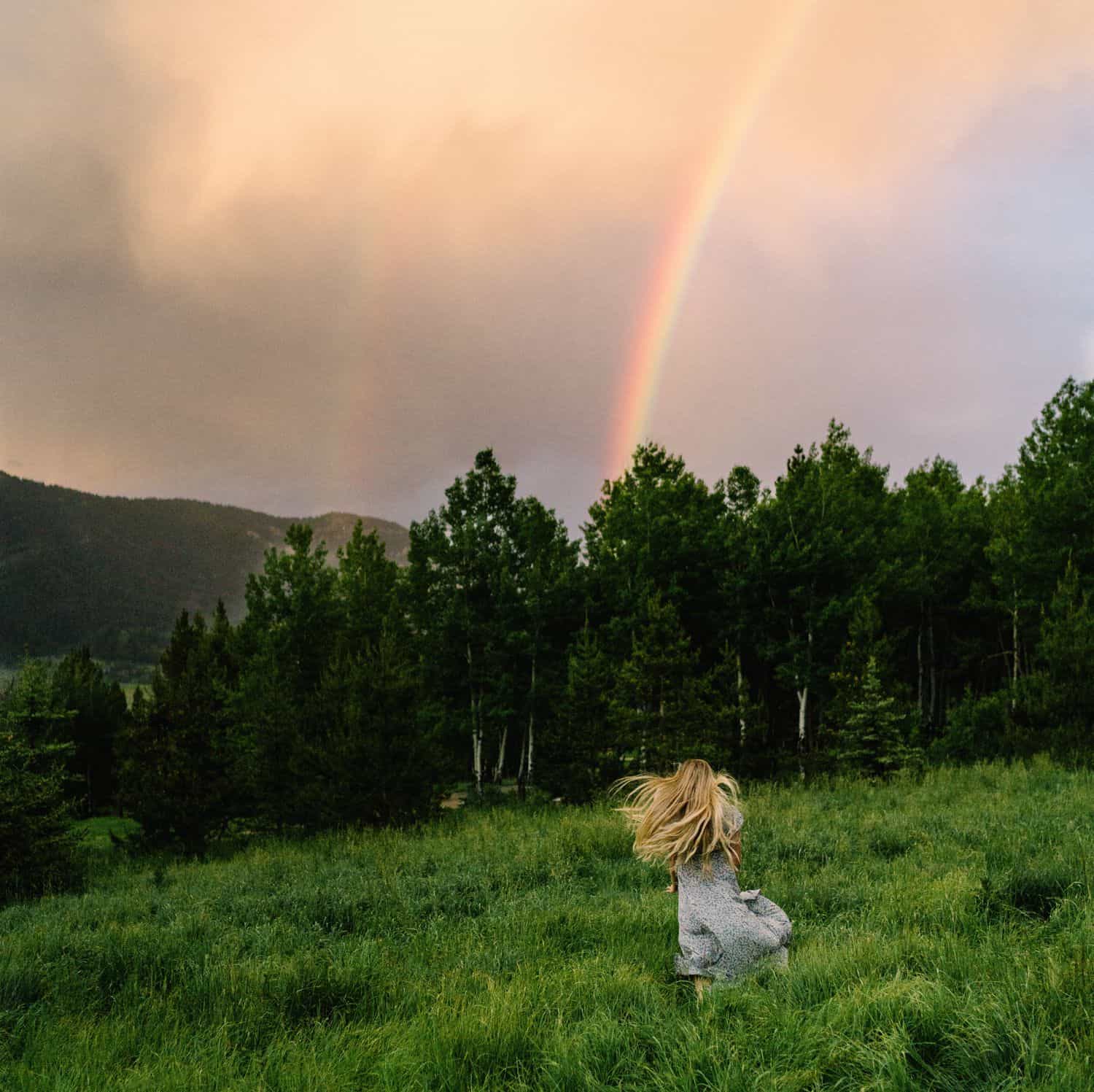 A senior girls runs through a lush green field toward a rainbow in a gloomy sky