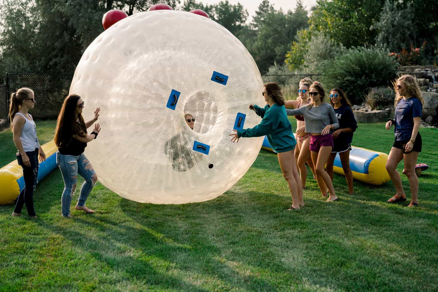 A group of senior girls play with a gigantic hamster ball in a newly-cut field of grass