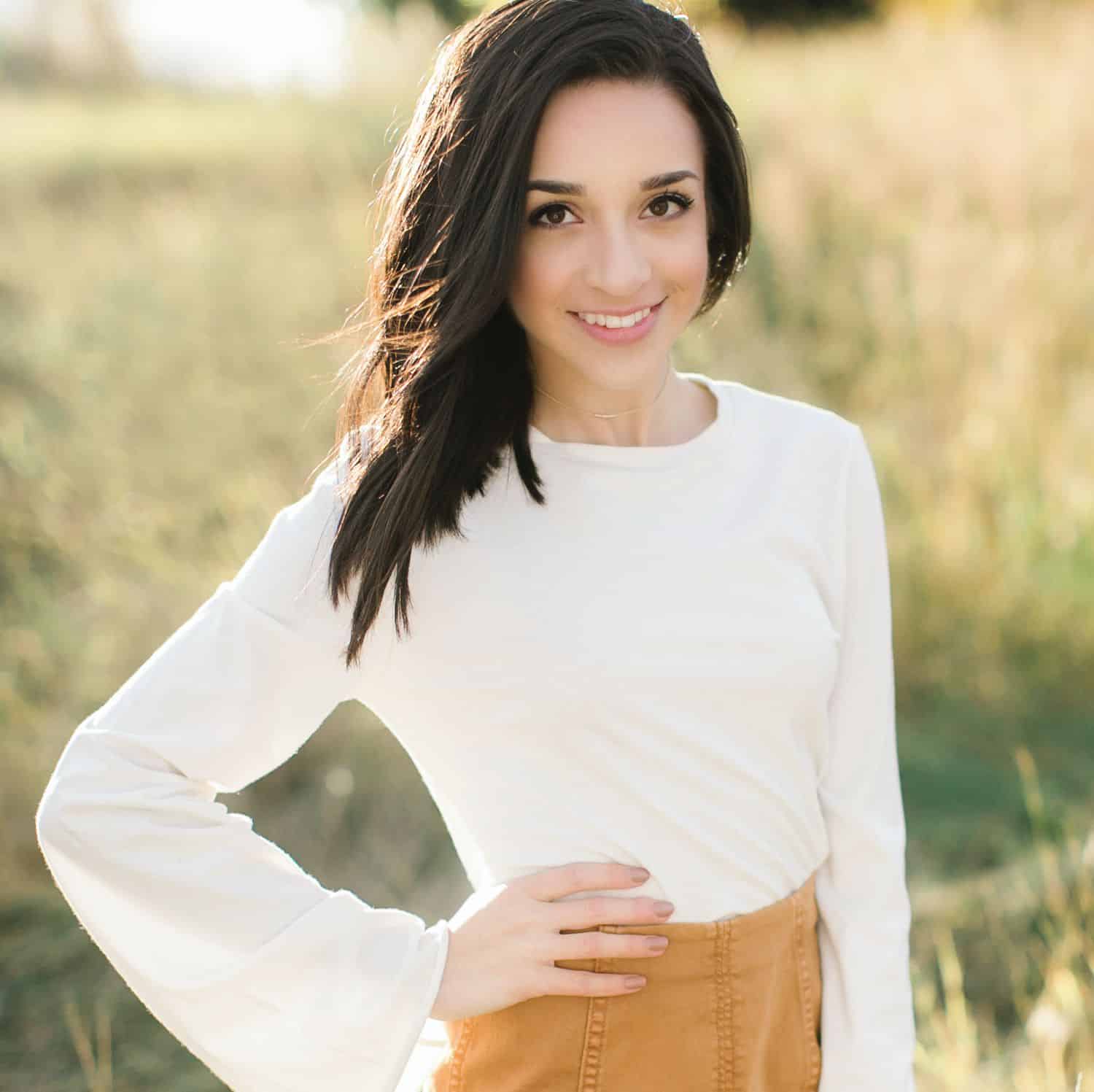 A senior girls stands in a field with one hand on her hip
