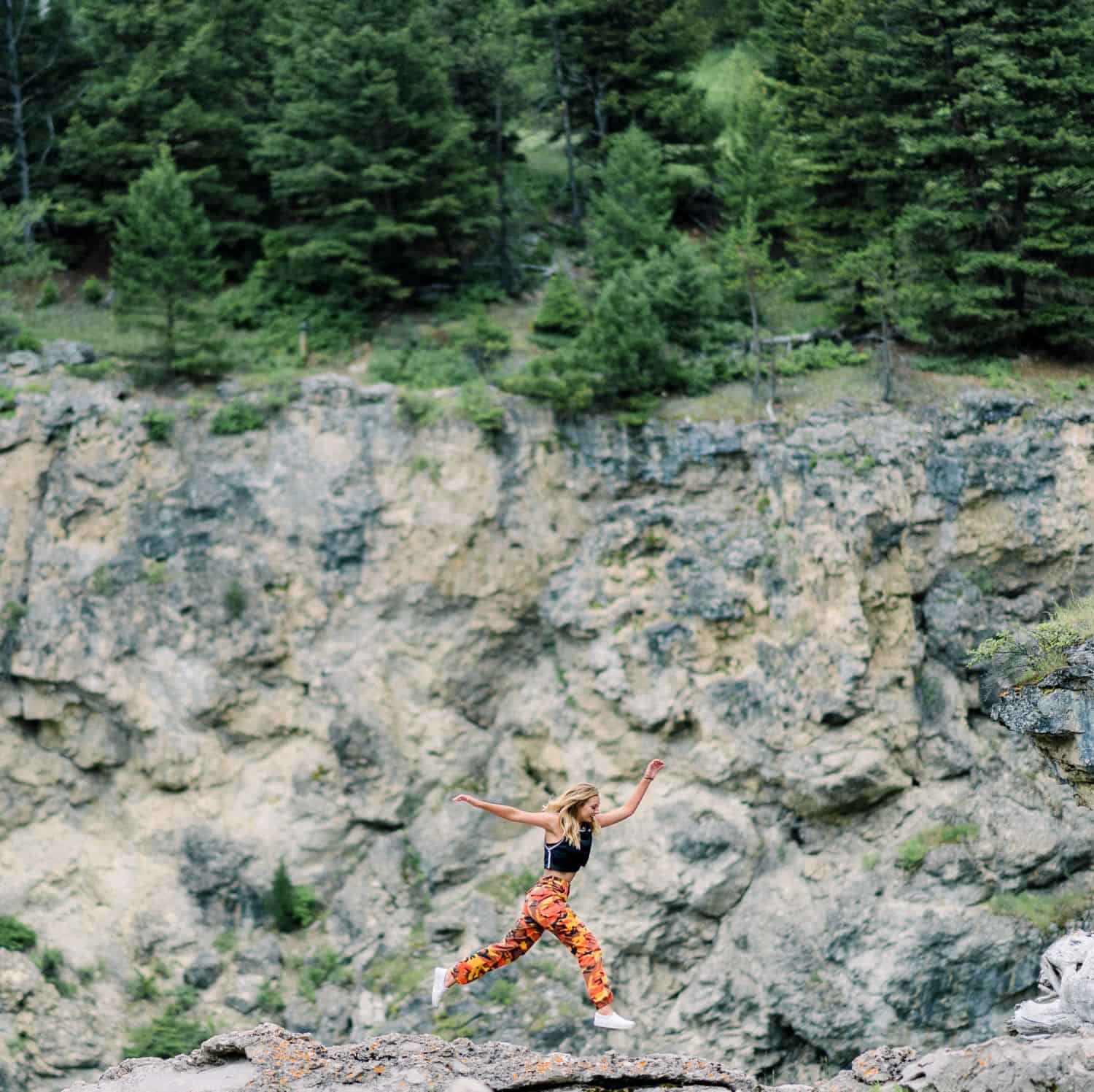 A senior girl leaps across rocks along the side of a cliff