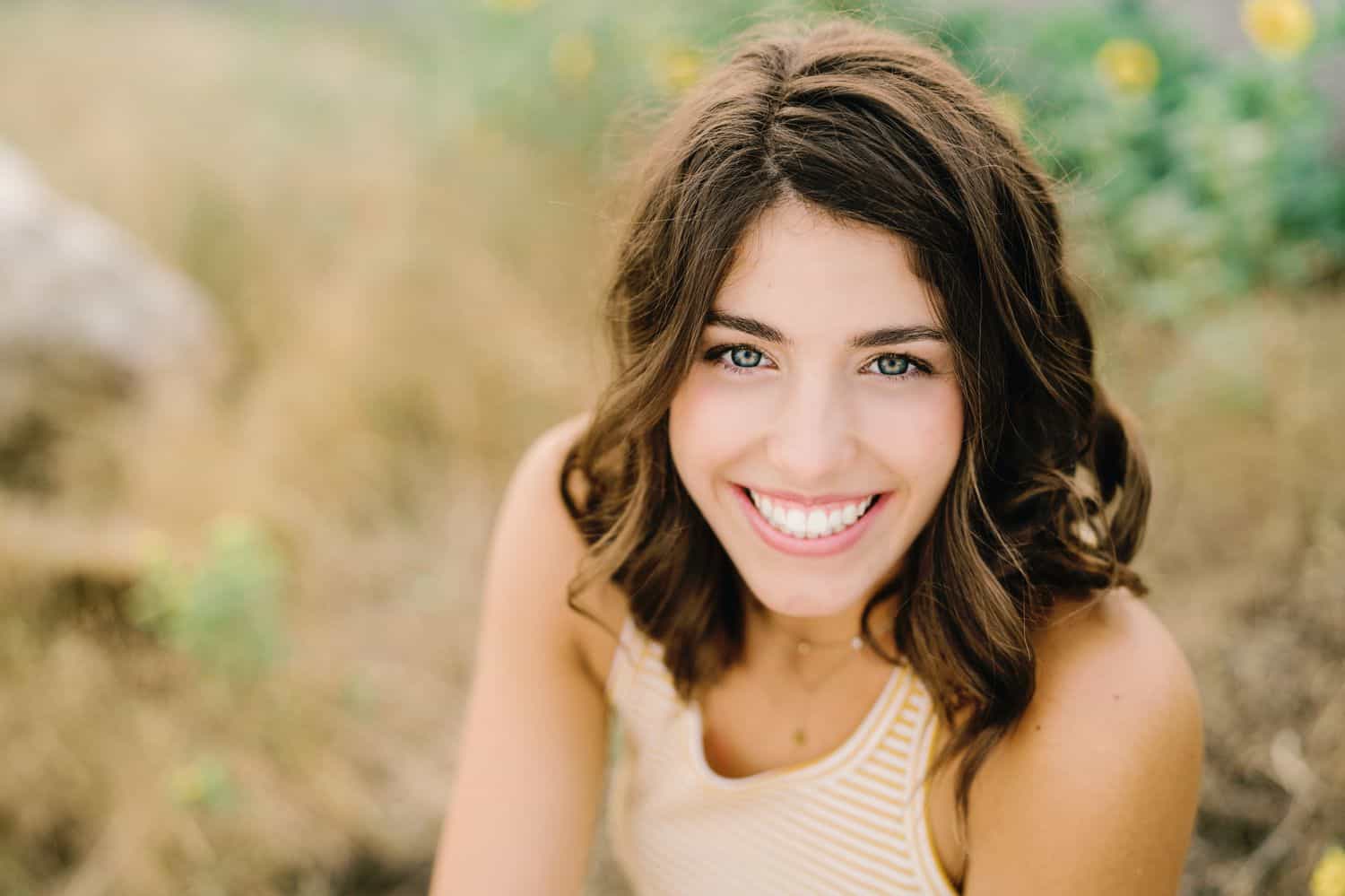 A senior girls sits in a field with a wide smile on her face