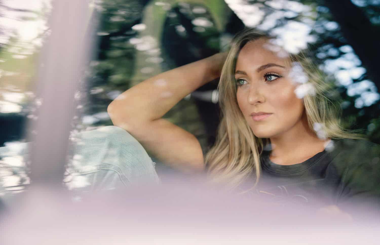 A senior girls is photographed through the reflection of a car window