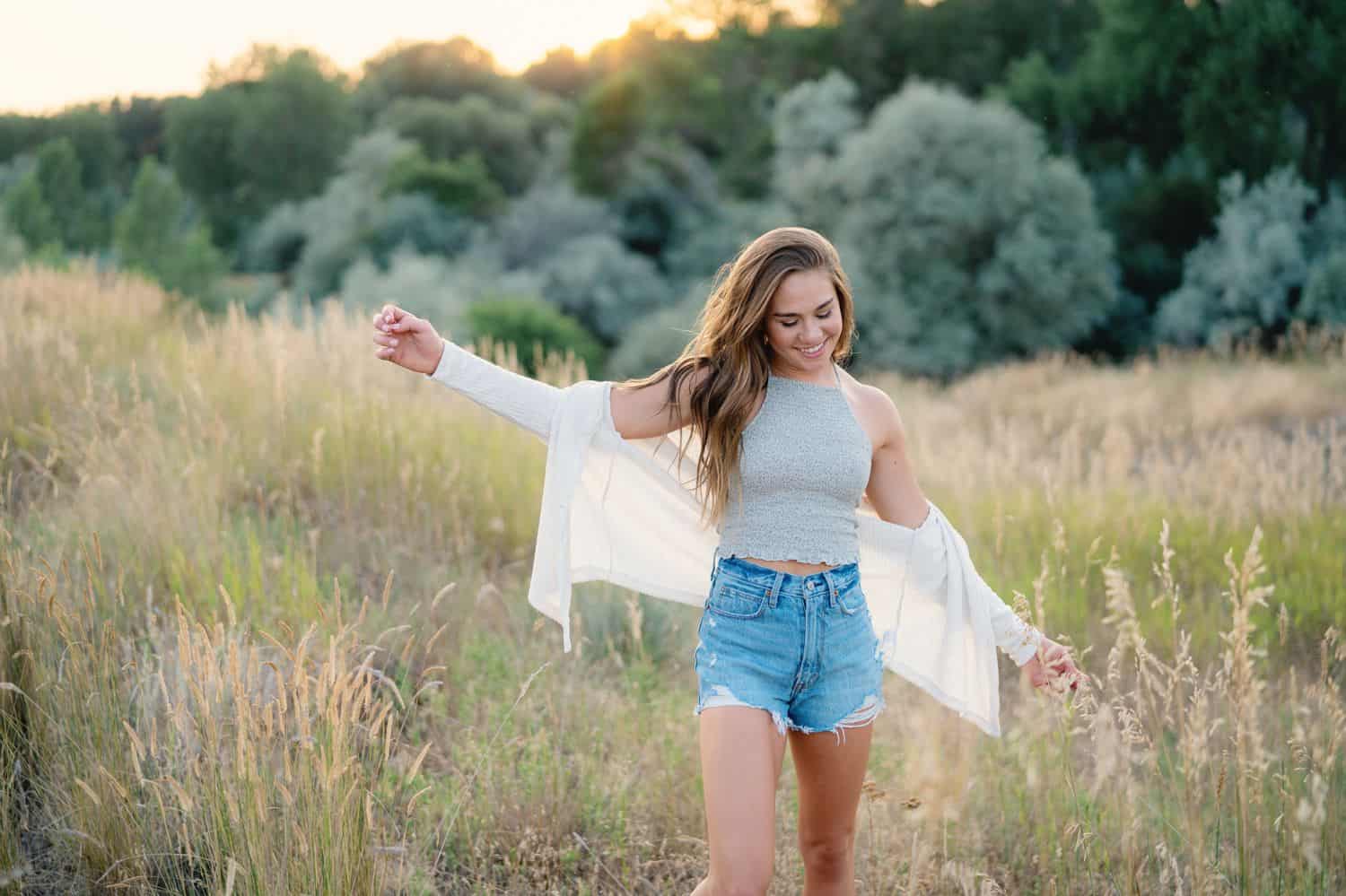 A senior girl walks through an overgrown field with her arms outstretched