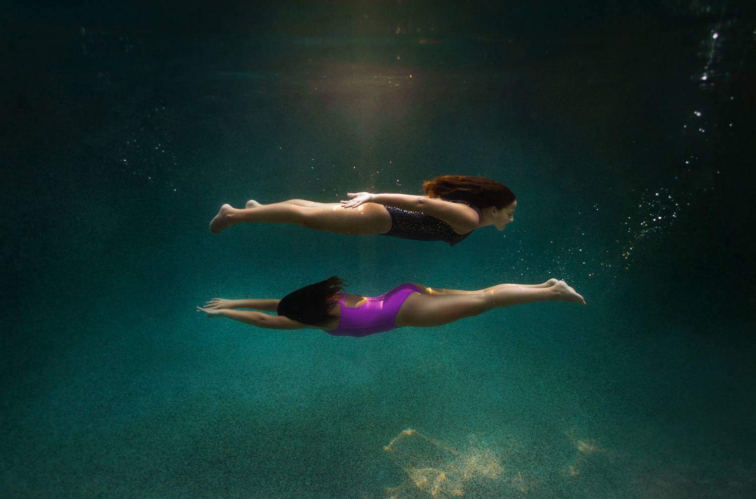 Two children swim underwater. One child is above the other, creating two parallel lines beneath the water