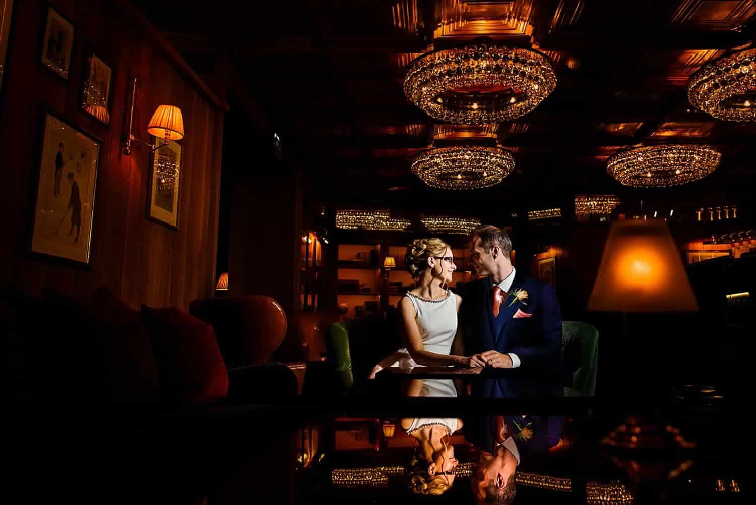 A bride and groom sit in a dark ballroom gazing into one another's eyes