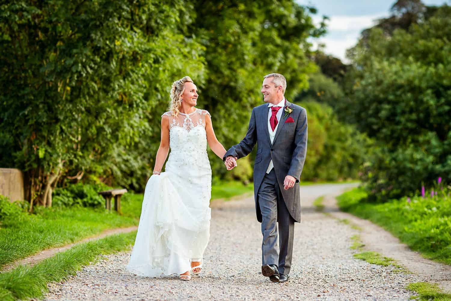 A bride and groom stroll outside down a garden path before their wedding