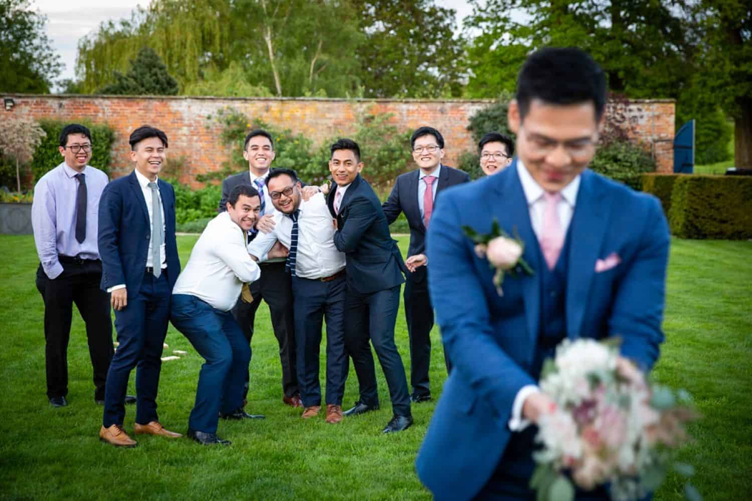 A groom holds a bouquet in a joking attempt to toss it to his groomsmen