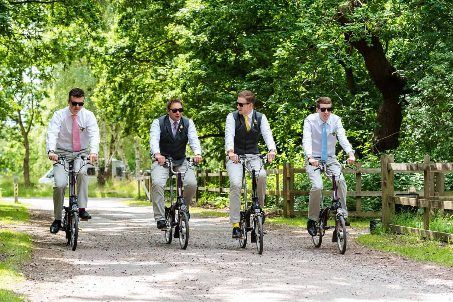 Groomsmen ride bicycles down a gravel path on the wedding day