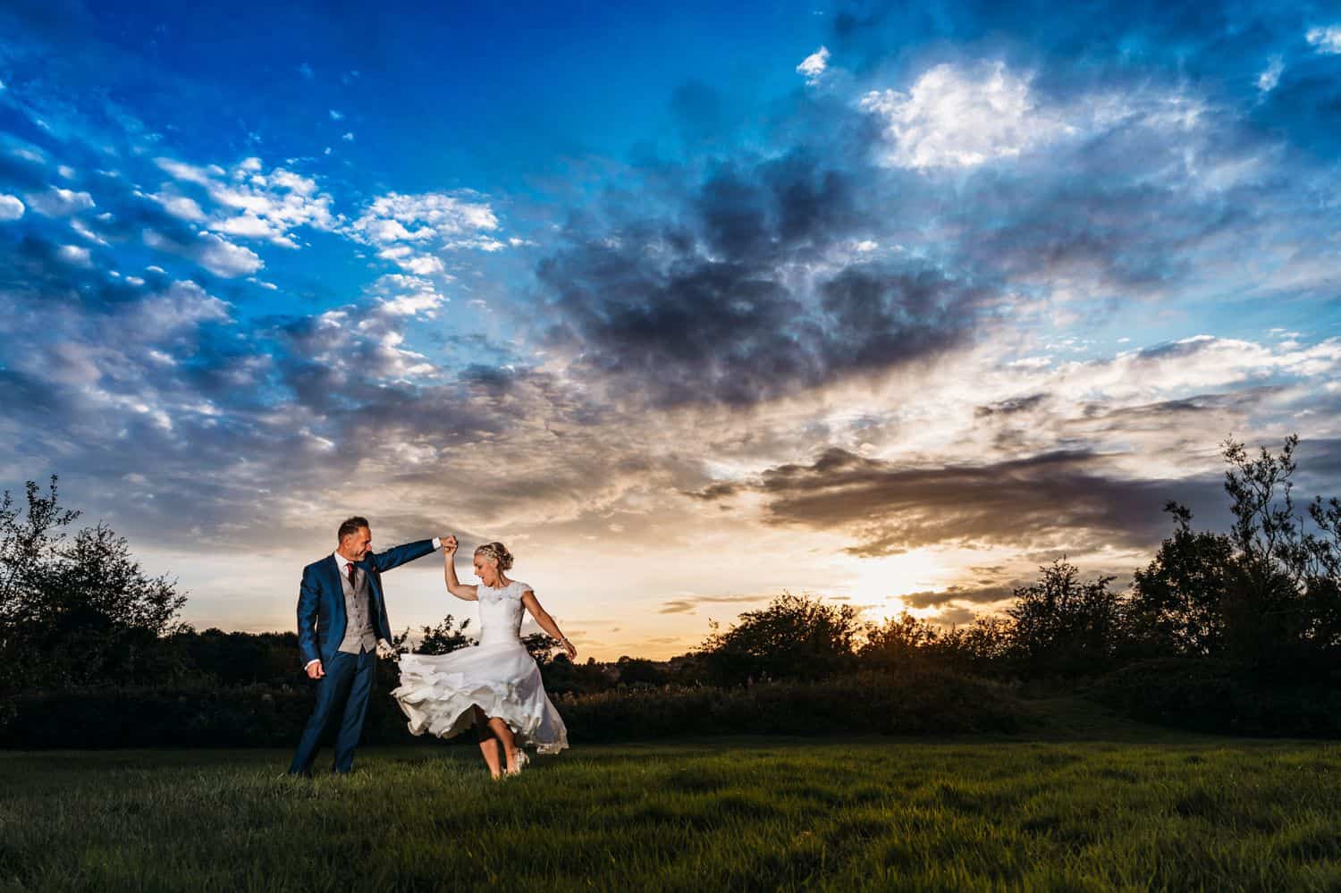 A sunset portrait of a groom twirling his bride in a wide lawn