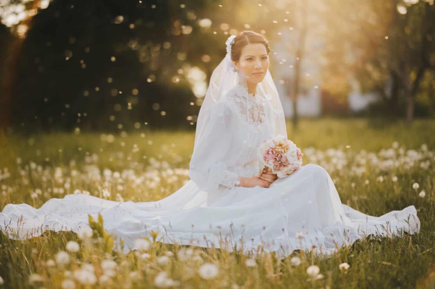 A bride kneels in a field for a sunset portrait