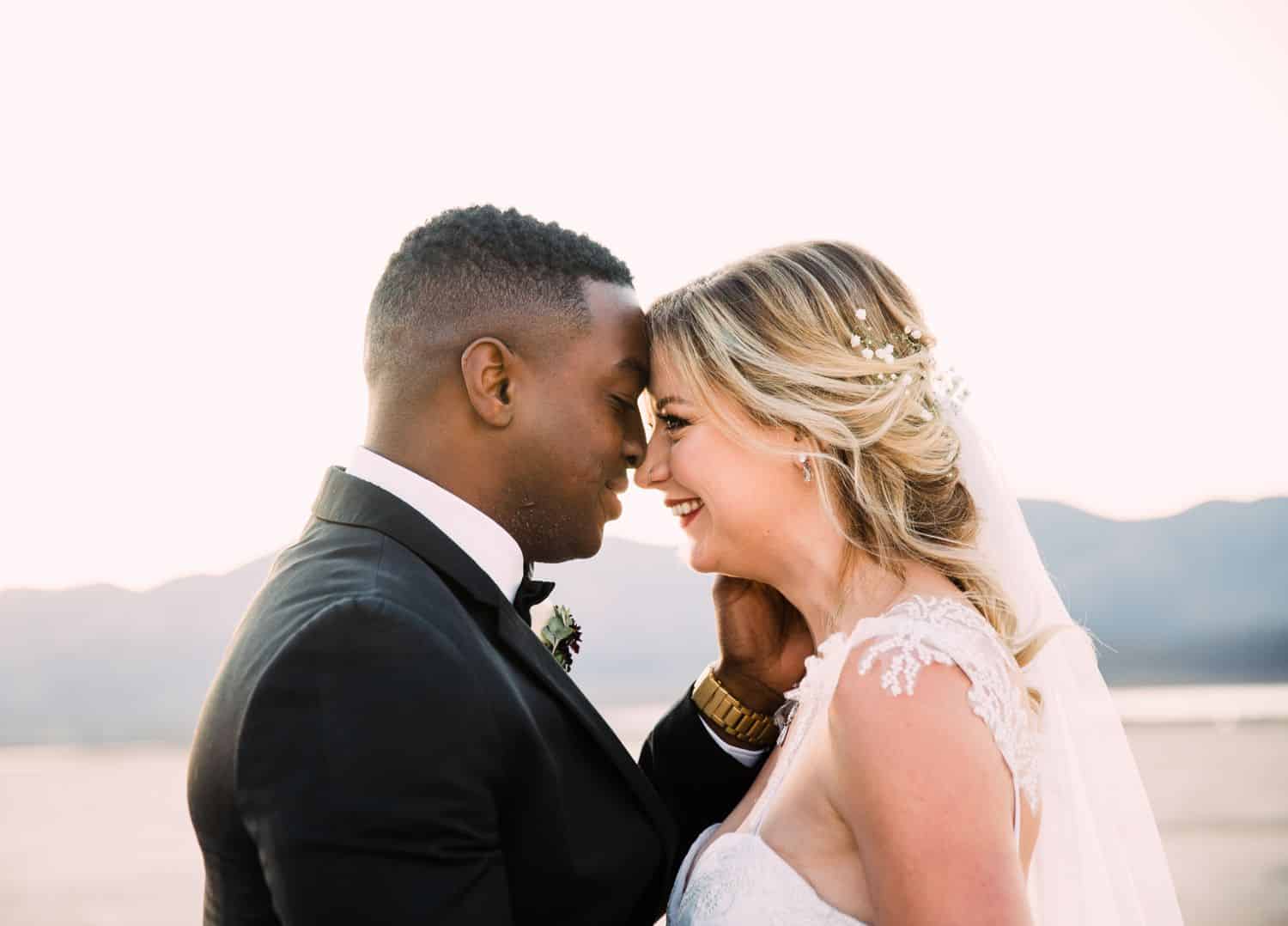 A bride and groom pose nose-to-nose while smiling for portraits after their desert wedding