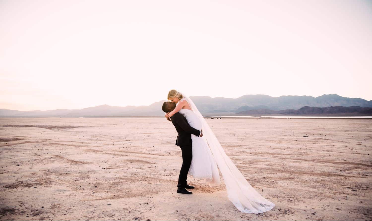 The groom lifts his bride into the air for a kiss after their desert ceremony