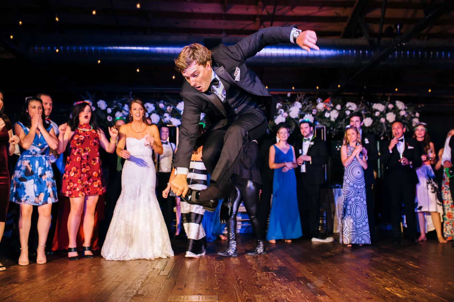 A groomsman leaps into the air in an impressive dance move during a wedding reception