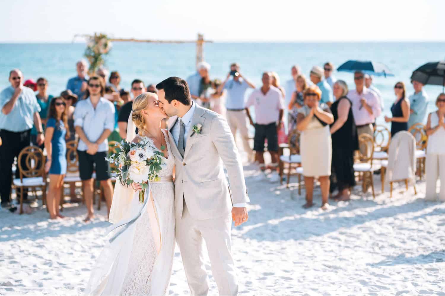 A bride and groom kiss after processing up the aisle after their wedding ceremony on the beach