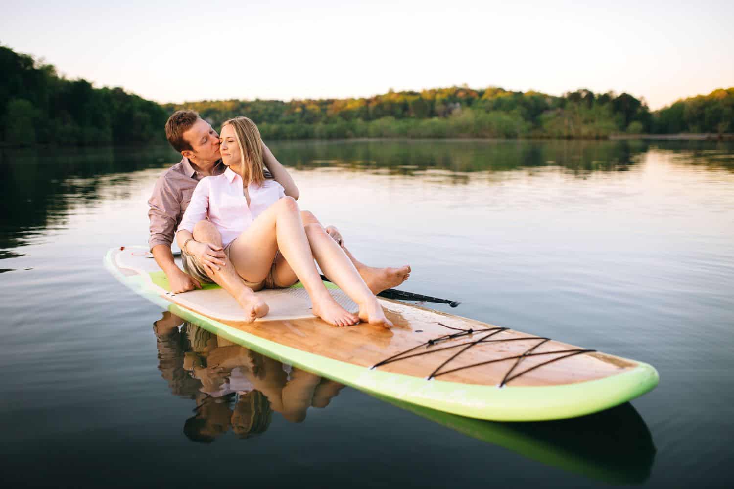 A couple sits on a paddleboard for their engagement photos